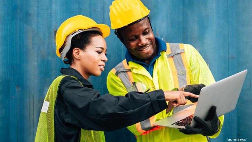 2 African American workers in hardhats look at computer