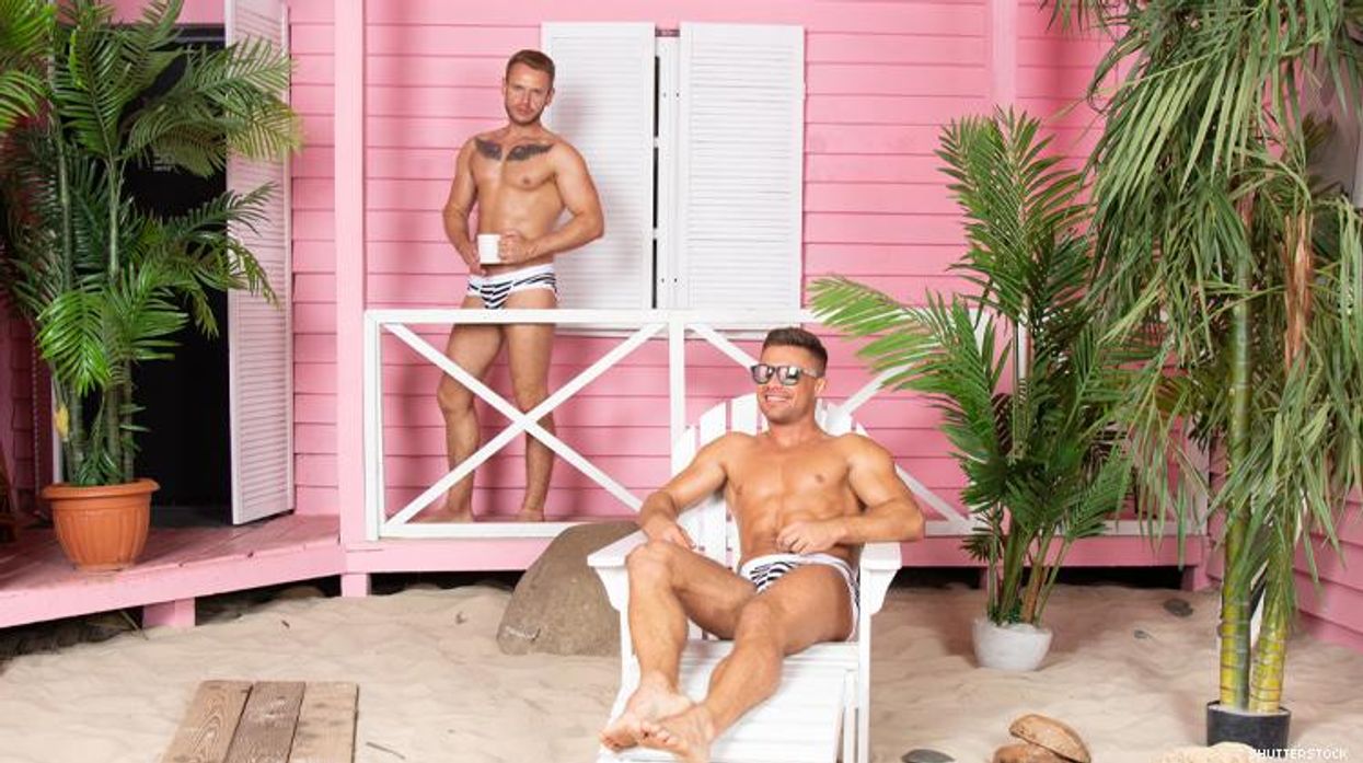 2 gay men in swimsuits in front of pink beach house