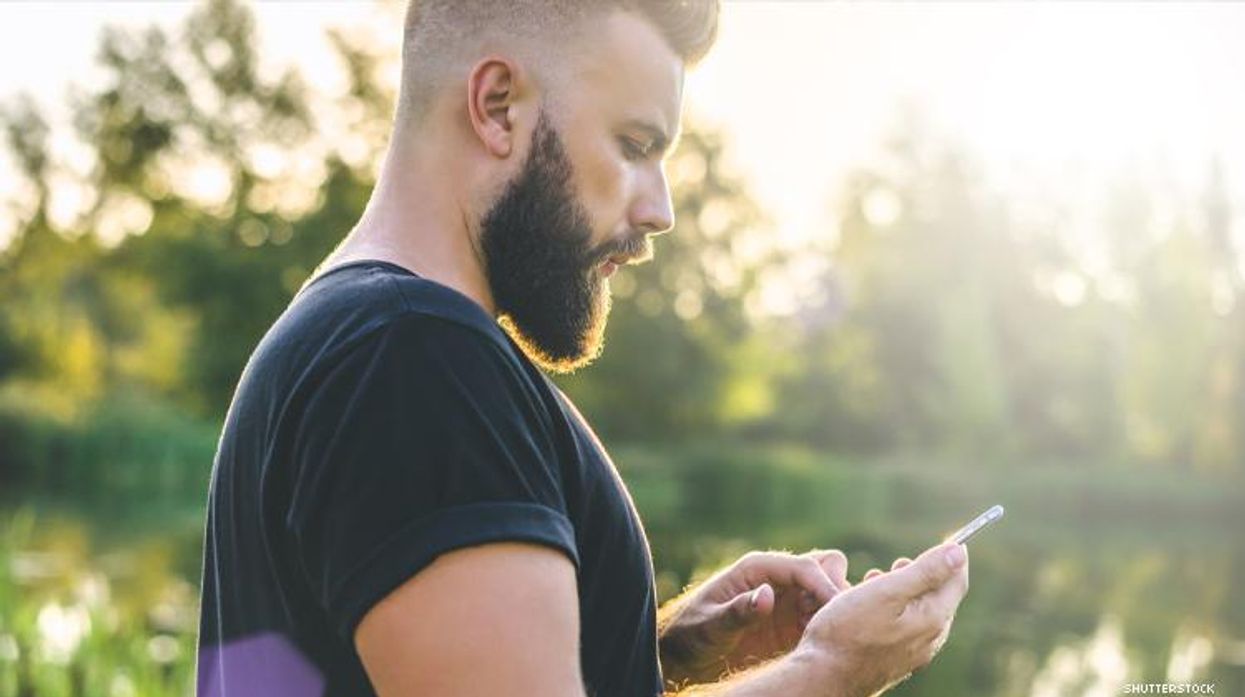 A cool man looks at his smart phone standing next to a lake