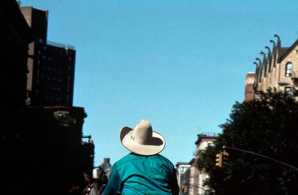 A man wearing a white cowboy hat rides a horse through a city street.