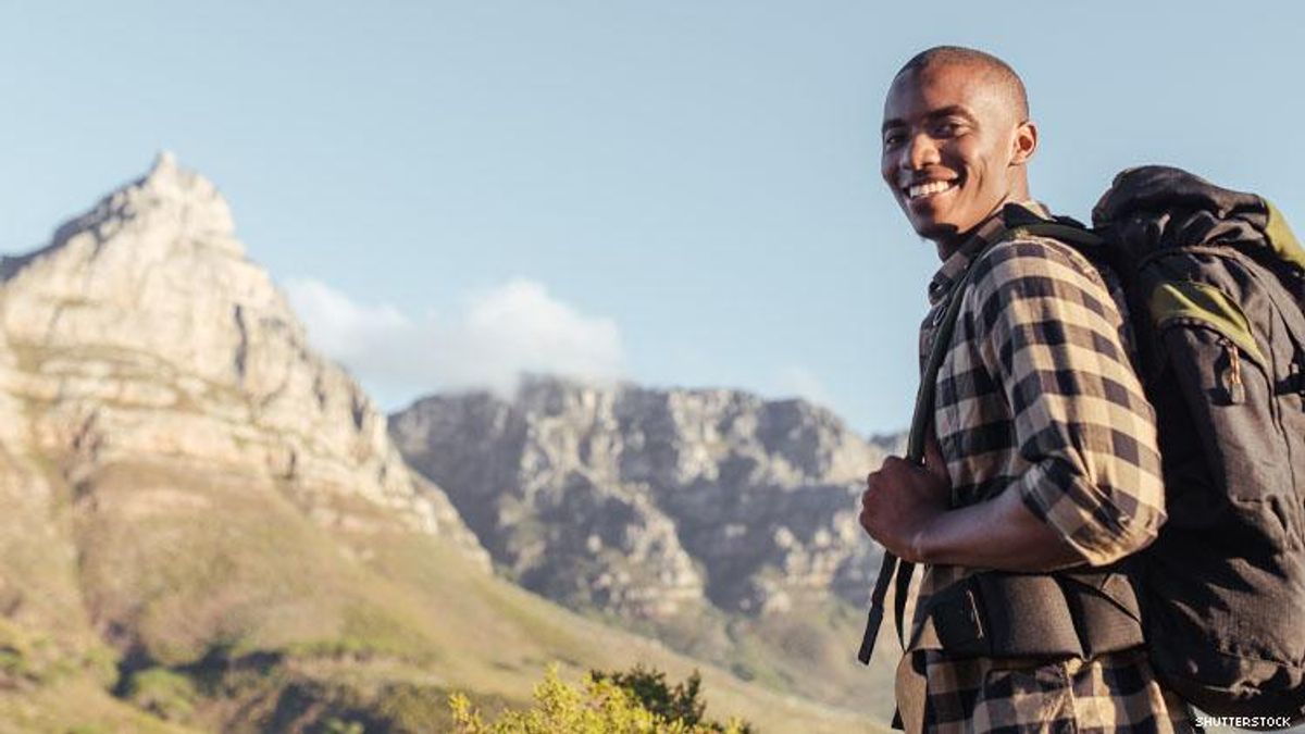 A smiling Black man hiking with mountains behind