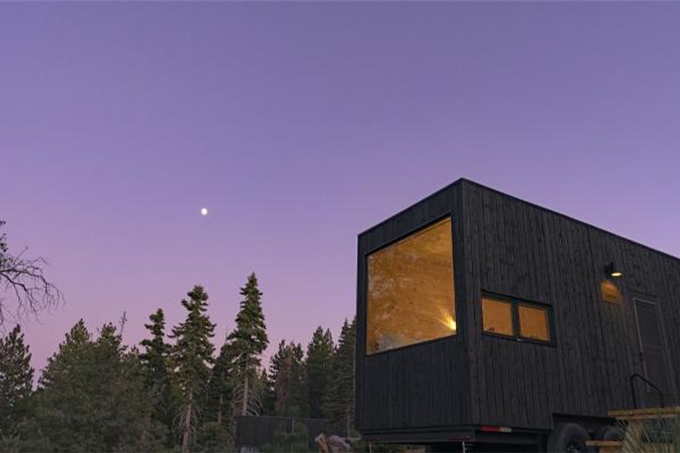 A tiny home with big window as darkness falls in woods