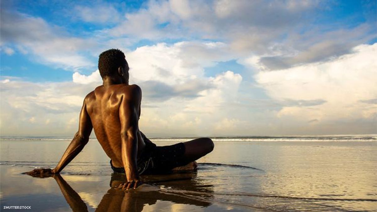 Black man sitting in water on beach