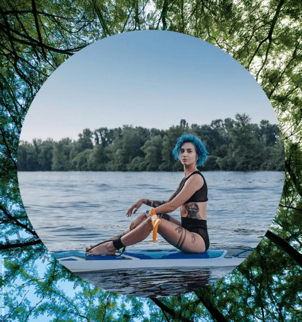 Blue haired woman in swimsuit on paddle board