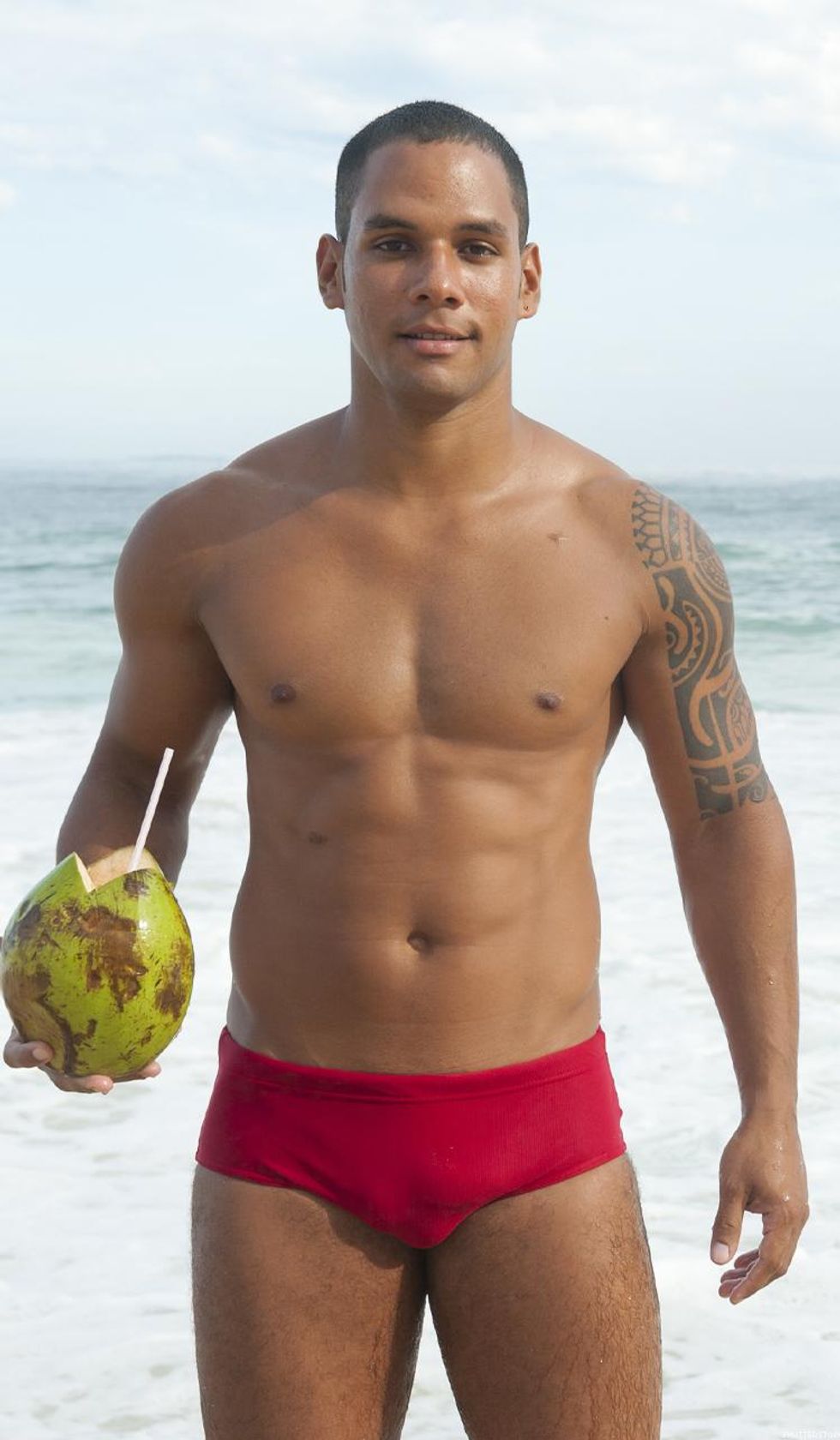 Brazilian man stands in the ocean holding a coconut drink
