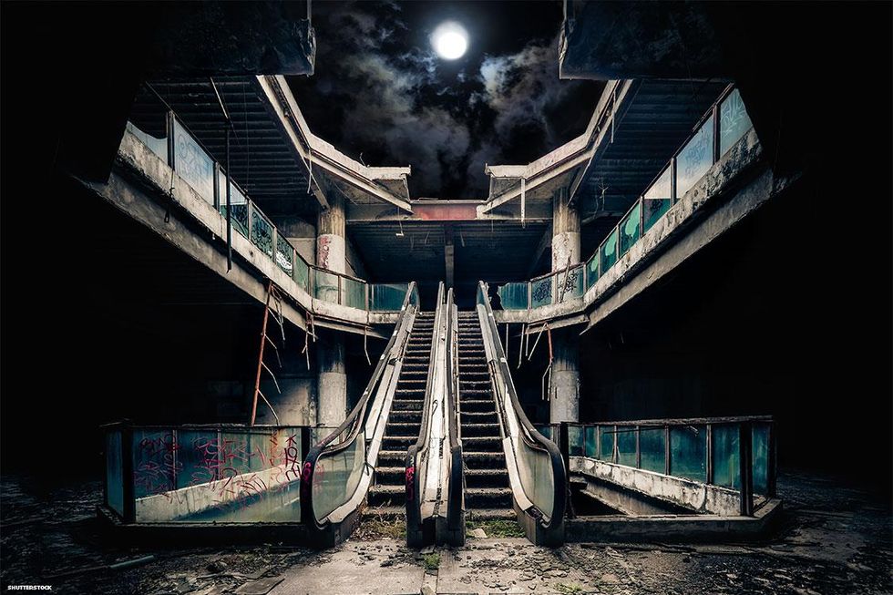 Escalator in an abandoned building at night, the roof collapsed and moon visible