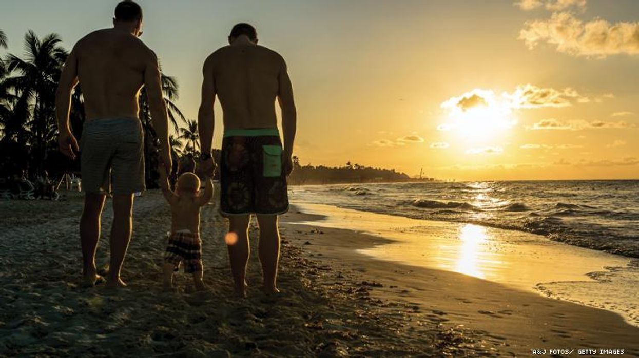 Gay couple walking along beach holding hands with their child