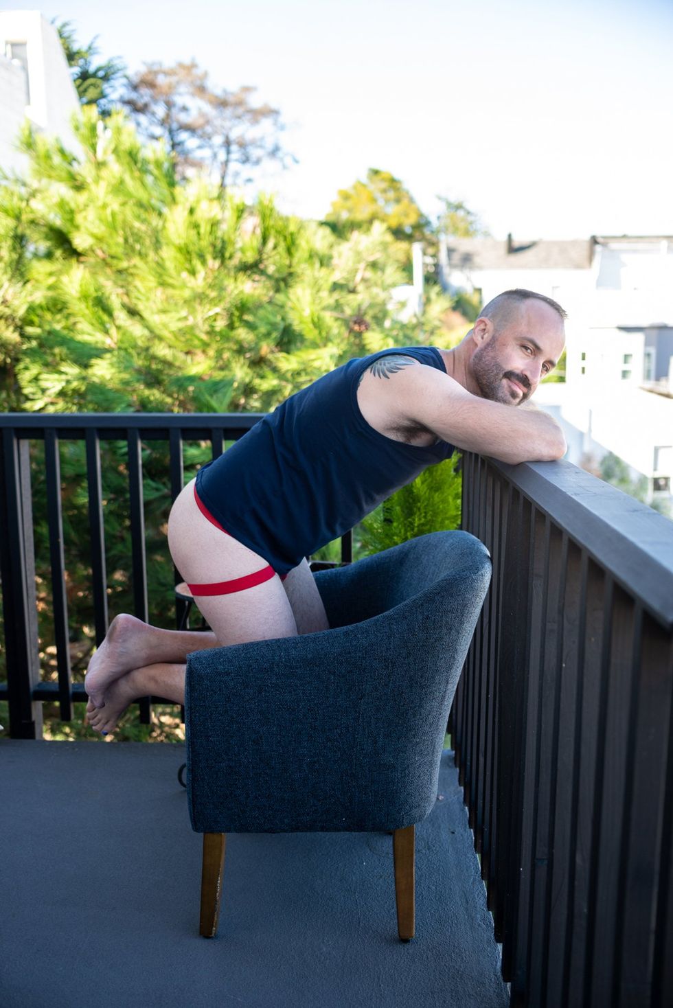 gay man wearing t-shirt and jock kneeling on chair on porch