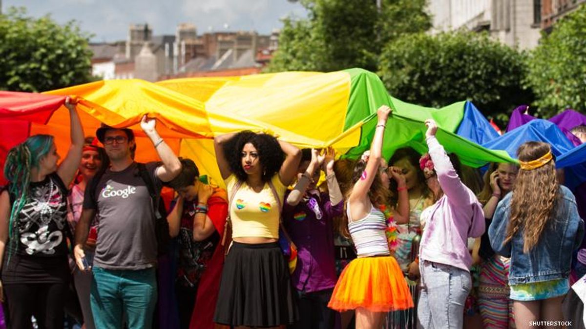 Group of LGBTQ people hold aloft a giant rainbow flag