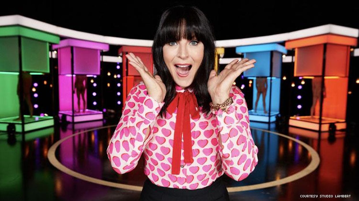 Host of Naked Attraction on stage featuring naked men in dimly lit pods