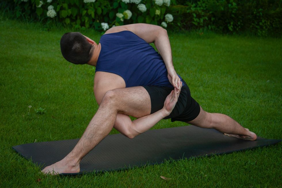 man in blue tank top and black shorts lying on black mat on green grass field