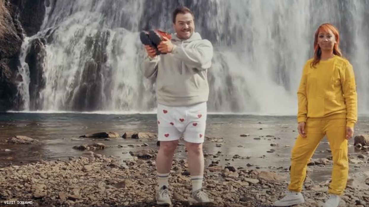 Man in boxer shorts holds aloft sweatpant boots next to rapper Cell7 both in front of an Icelandic waterfall