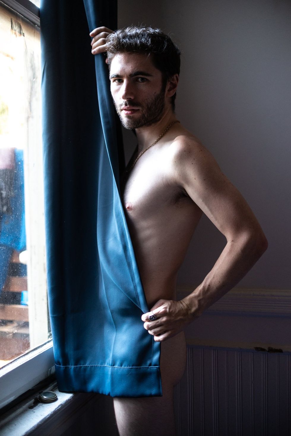 Man stands in front of window, naked but covered by curtain