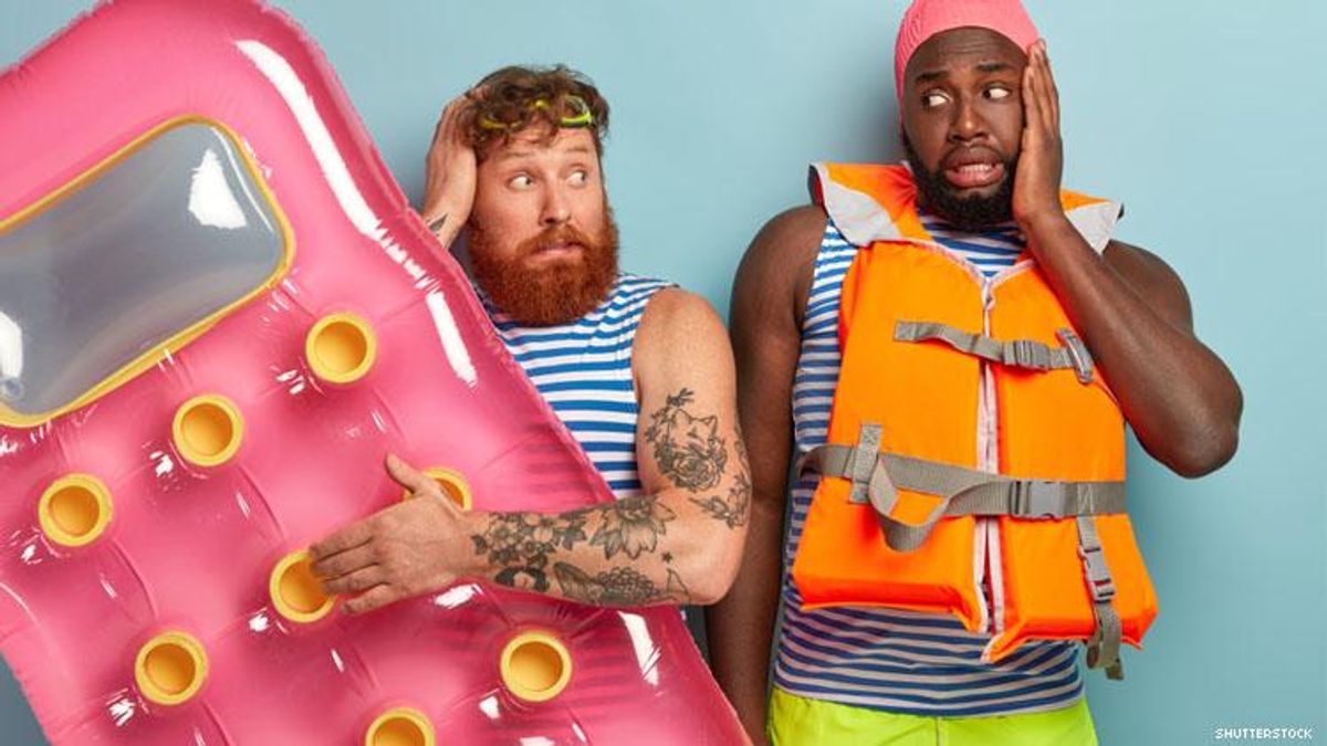Mixed race gay couple summer clothes, one with life jacket other a pool float, they look nervous