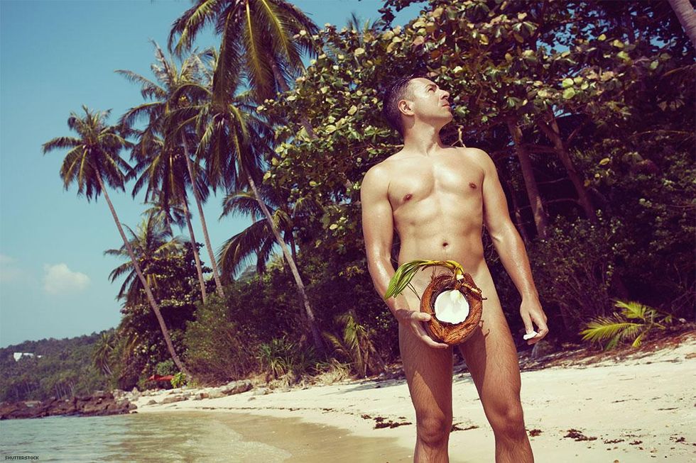 Naked man holding a coconut on a beach with palm trees