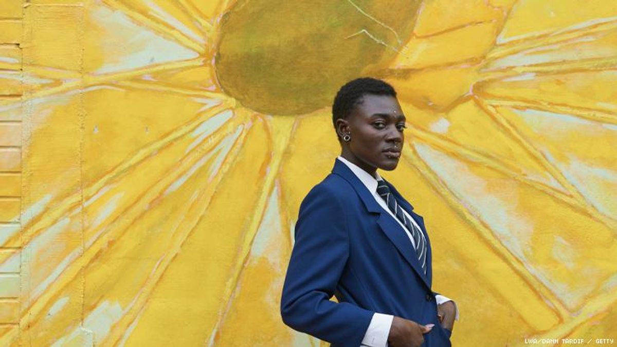 Nonbinary Black person in suit in front of a bright sunflower mural