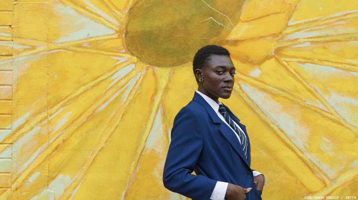 Nonbinary Black person in suit in front of a bright sunflower mural