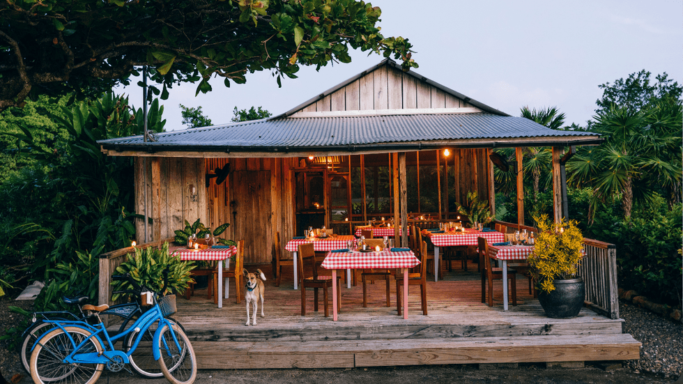 Open-air wooden restaurant at Turtle Inn with red-checkered tablecloths, candlelit tables, and a blue bicycle parked outside.