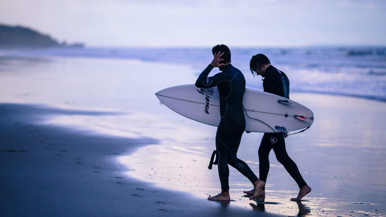 person walking on seashore holding surfboard