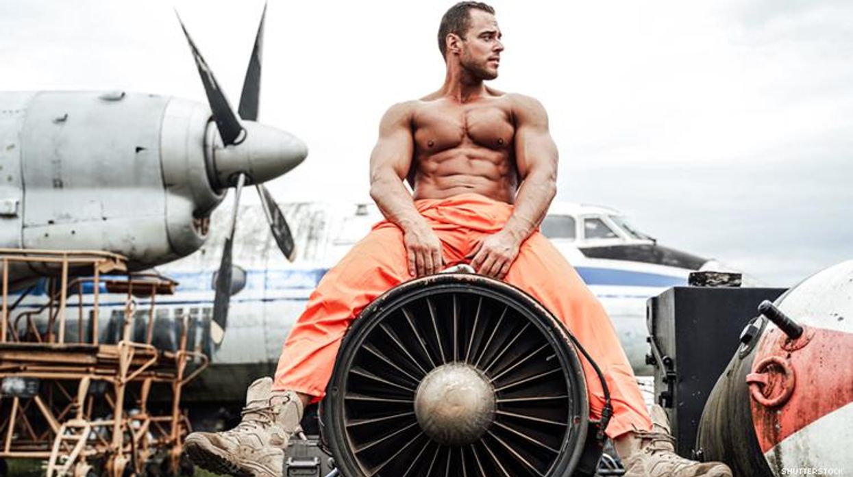 Shirtless man sits on a plane's engine with airplane behind him