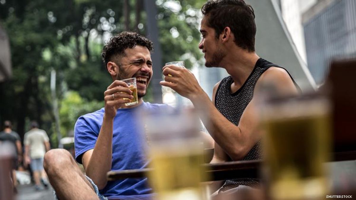 Two gay men of color toast at an outdoor bar