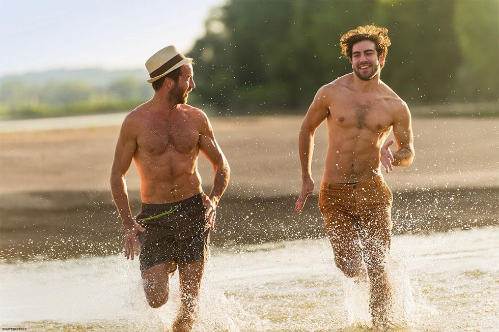 Two shirtless men one wearing shorts and the other wearing jeans running through the surf