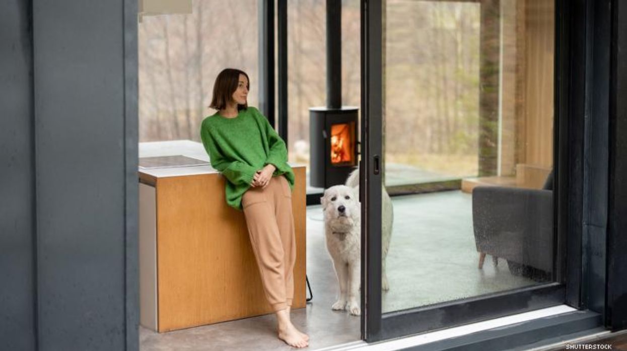 Woman and white dog in forest home with floor to ceiling windows and wood stove