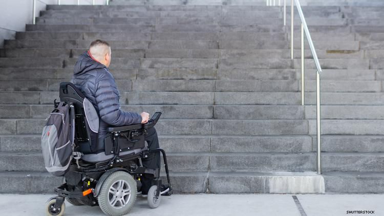 Disabled man using wheelchair, at bottom of flight of stairs