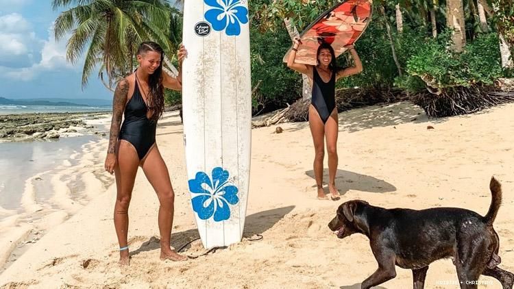lesbian couple with surfboards and a dog on a beach