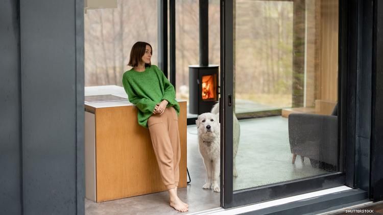 Woman and white dog in forest home with floor to ceiling windows and wood stove