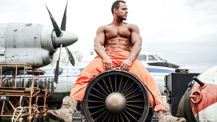 Shirtless man sits on a plane's engine with airplane behind him