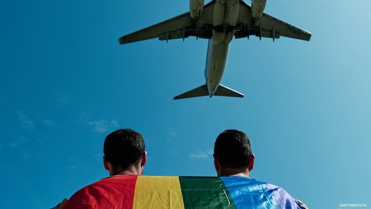 Airplane flies over a queer couple draped in a rainbow flag