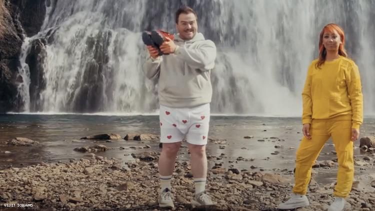 Man in boxer shorts holds aloft sweatpant boots next to rapper Cell7 both in front of an Icelandic waterfall