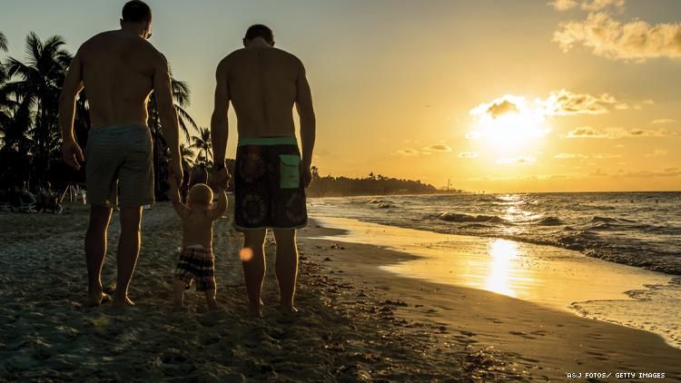 Gay couple walking along beach holding hands with their child